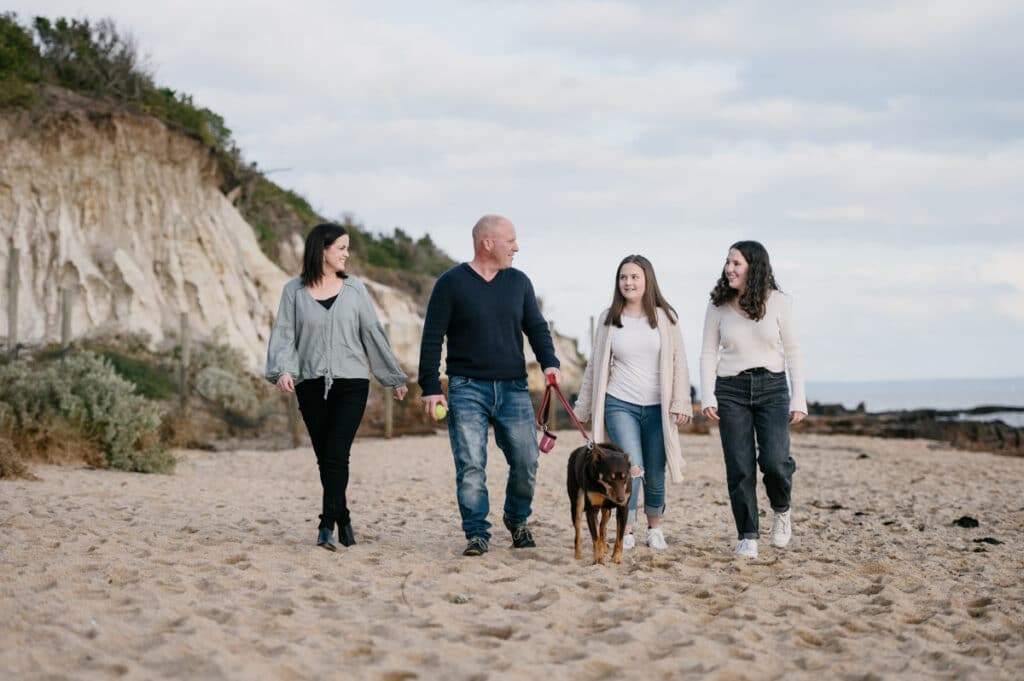 Family rugged up for the Melbourne winter school holidays walking on a Bayside beach